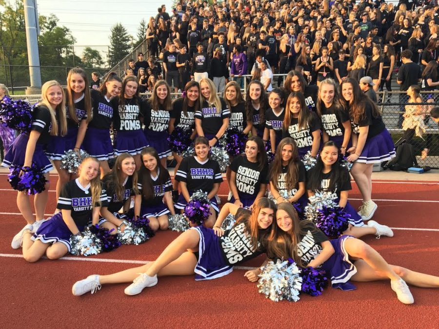 Varsity poms team poses with the student section at football game.