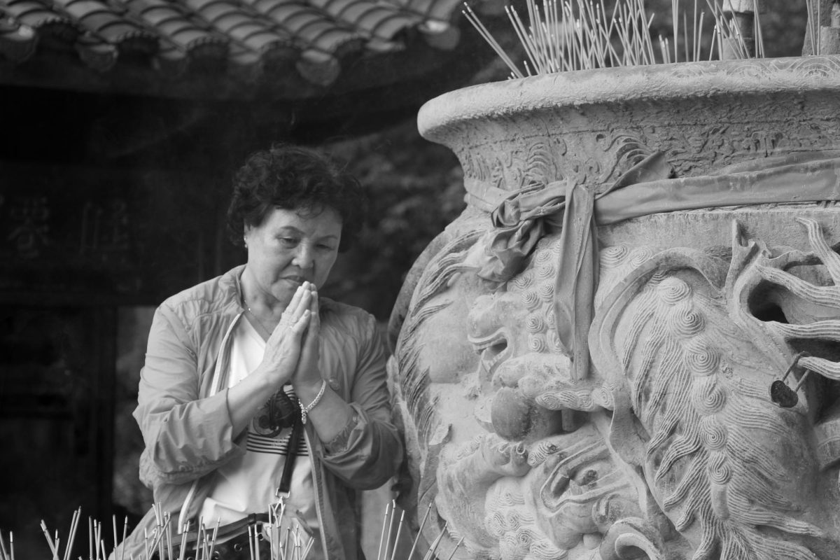 An old woman in Zhangjiajie, China, says a prayer beside an incense burner.